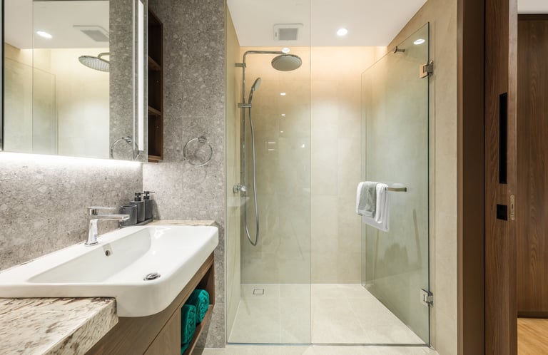 Modern bathroom with white sink, large mirror, tile backsplash, and glass-enclosed walk-in shower with rainfall showerhead