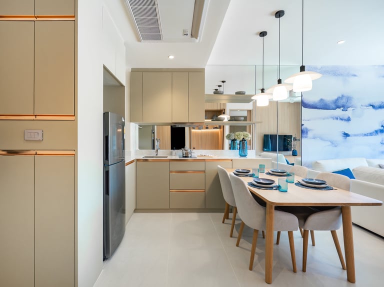 Modern kitchen and dining room with beige cabinetry, wooden dining table, pendant lights, and blue landscape artwork on window
