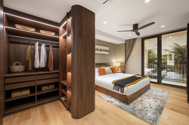 Modern bedroom with walk-in wooden wardrobe, bed with orange and blue accents, hardwood flooring, ceiling fan, and sliding glass doors to balcony