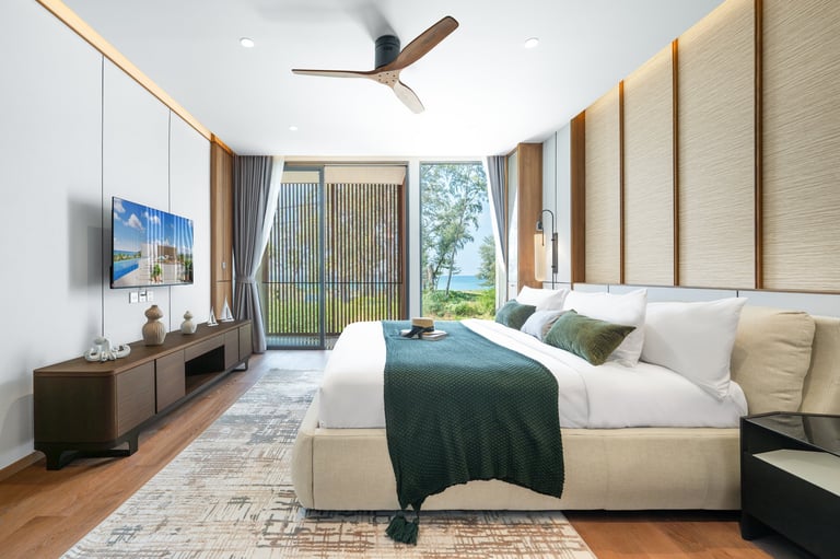 Modern bedroom with beige upholstered headboard, green bedding, ceiling fan, dark wood TV console, and glass doors opening to outdoor view