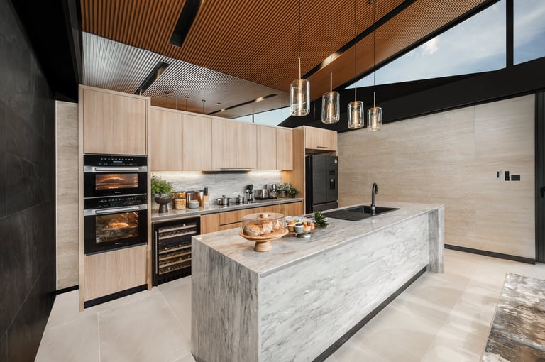 Modern kitchen with light wood cabinetry, marble island, black appliances, and wooden ceiling detail
