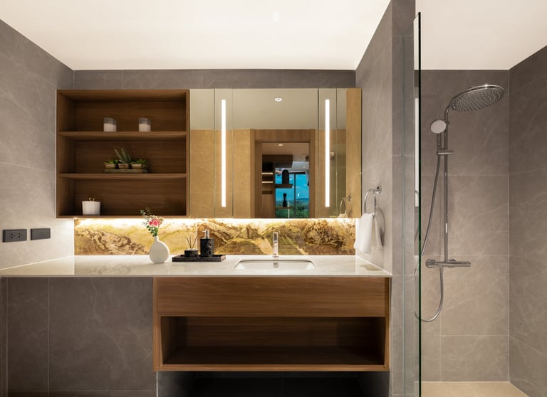 Modern bathroom vanity with wooden cabinetry, illuminated mirror, white countertop, and walk-in shower area with gray tile walls