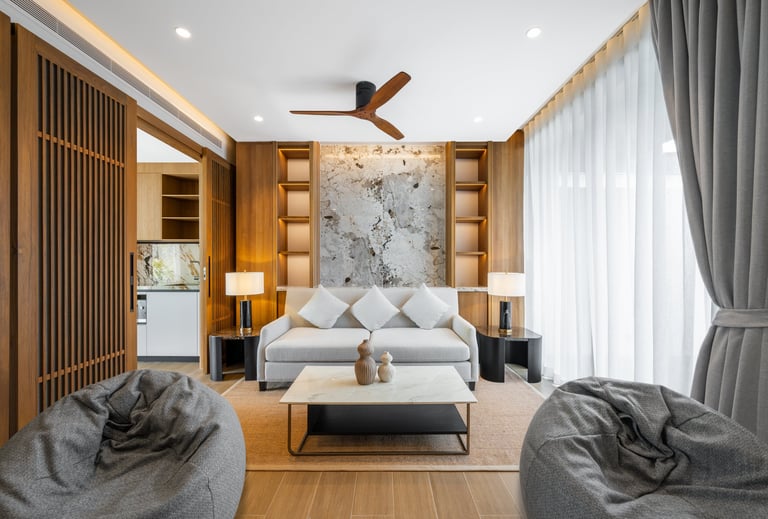 Modern bedroom with wooden paneling, gray upholstered bed, marble accent wall, ceiling fan, and comfortable seating areas with gray bean bags