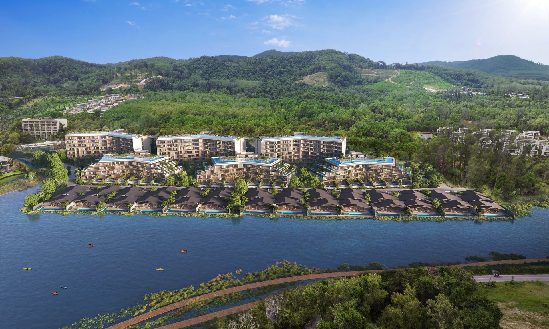 Aerial view of waterfront residential complex with multi-story buildings, trees, and green mountains in the background
