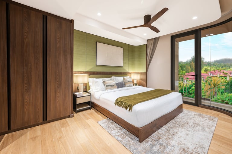 Modern bedroom with queen bed, green accent wall, dark wood wardrobe, wooden flooring, ceiling fan, and large glass doors overlooking landscaped garden