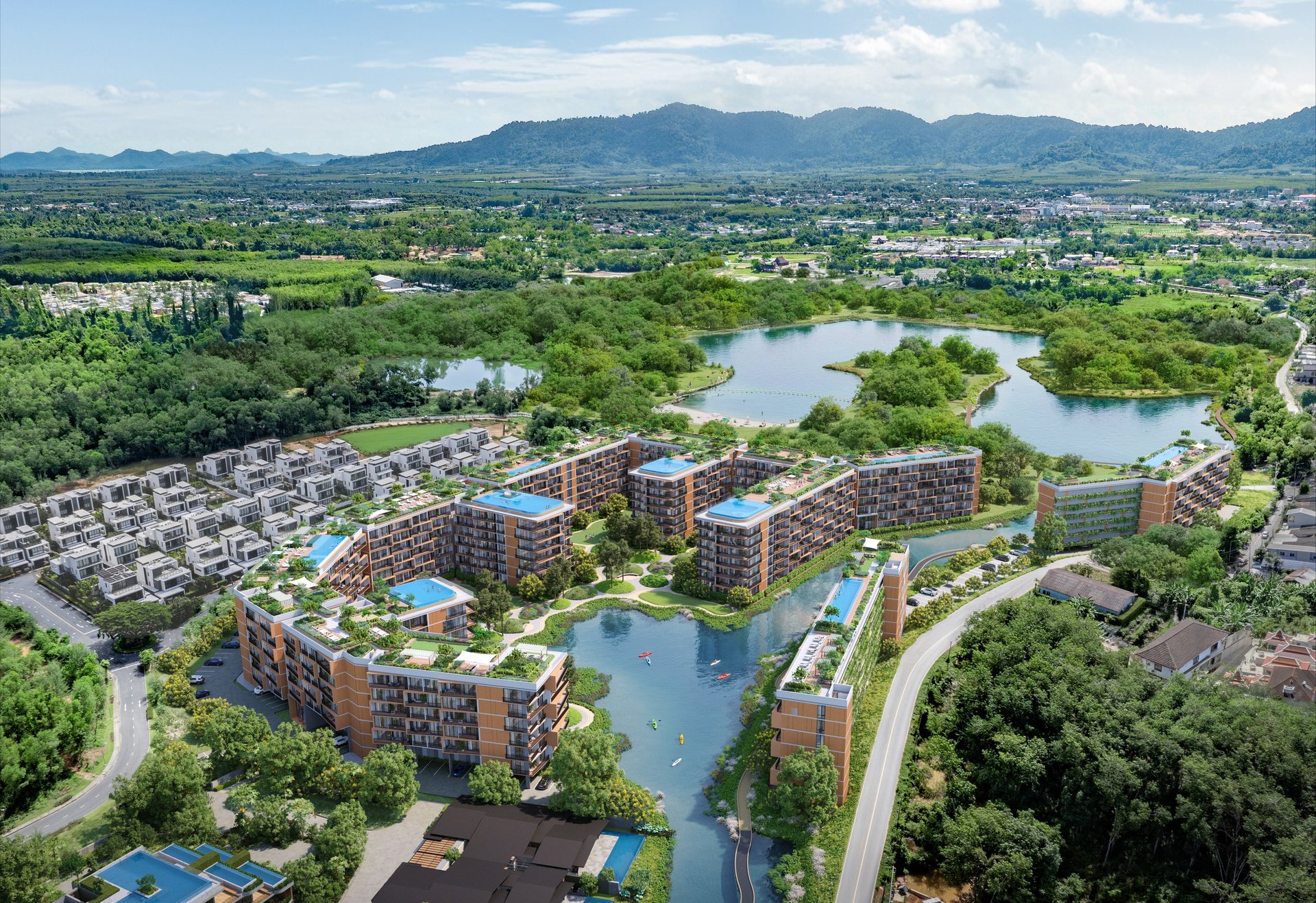 Aerial view of a modern residential development with apartment buildings surrounding artificial ponds, set in a lush green valley with mountains in the distance