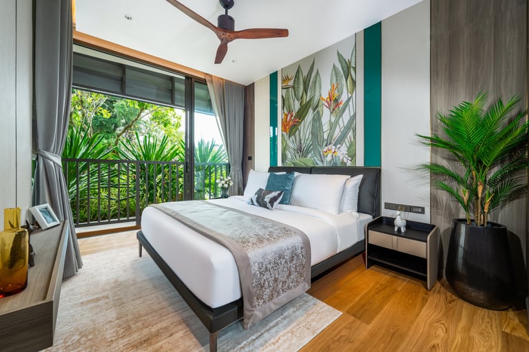 Modern bedroom with queen bed, green accent wall, potted plants, wooden floor, and balcony overlooking tropical garden view